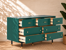 Load image into Gallery viewer, Image 4 of 4: A mid-century modern dresser with a teal green painted exterior, natural wood drawer interiors, and brass hardware, shown in a styled room setting with a white brick wall and plant.
