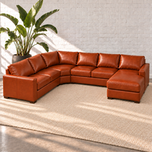 Load image into Gallery viewer, Image 5 of 14: Simulated Hollis 146-by-116-inch four-piece sectional in Mont Blanc Caramel leather with a corner wedge and integrated right chaise, styled with a plain ivory rug and bird-of-paradise plant.
