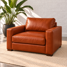 Load image into Gallery viewer, Image 1 of 4: Simulated Hollis 41-inch armchair in Mont Blanc Caramel leather with slim track arms, shown at a front angle on a plain ivory rug beside a bird-of-paradise plant against white brick.
