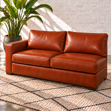 Load image into Gallery viewer, Image 13 of 14: Simulated Hollis 67-inch left-arm condo sofa in Mont Blanc Caramel leather with two seat cushions, two back cushions and open right side, styled with an ivory rug and bird-of-paradise plant.
