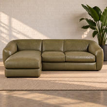 Load image into Gallery viewer, Image 2 of 8: Lucero olive-toned leather sectional with a continuous left-facing chaise and two sofa seats in a sunlit white-brick room.
