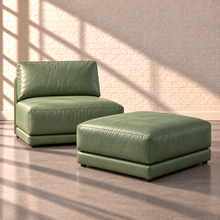 Load image into Gallery viewer, Image 2 of 3: Simulated Orinda armless chair with one separate square bumper ottoman in sage green Sequoia Rainforest leather, styled against white brick in natural sunlight.
