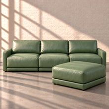 Load image into Gallery viewer, Image 2 of 6: Simulated Orinda three-piece sofa with one separate square bumper ottoman in sage green Sequoia Rainforest leather, against white brick in natural sunlight.

