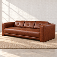 Load image into Gallery viewer, Image 4 of 6: Simulated right front angle of the Sullivan sofa in Crystal Ranch brown leather, showing the outer arm, tailored seat and button-tufted back against a white brick wall.
