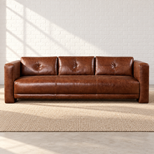 Load image into Gallery viewer, Image 1 of 6: Simulated front view of the Sullivan sofa in Crystal Ranch brown leather, with button-tufted back and tailored arms, against a white brick wall on a beige woven rug.
